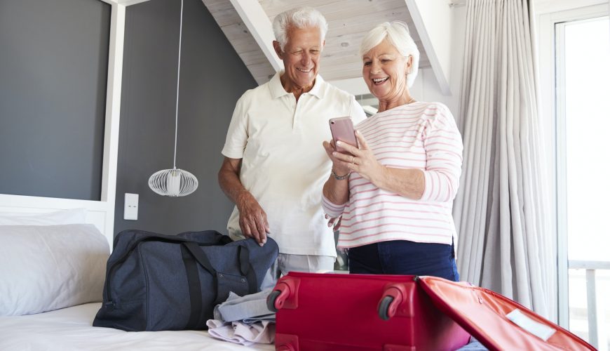 Senior Couple Look At Mobile As They Check In To Vacation Rental